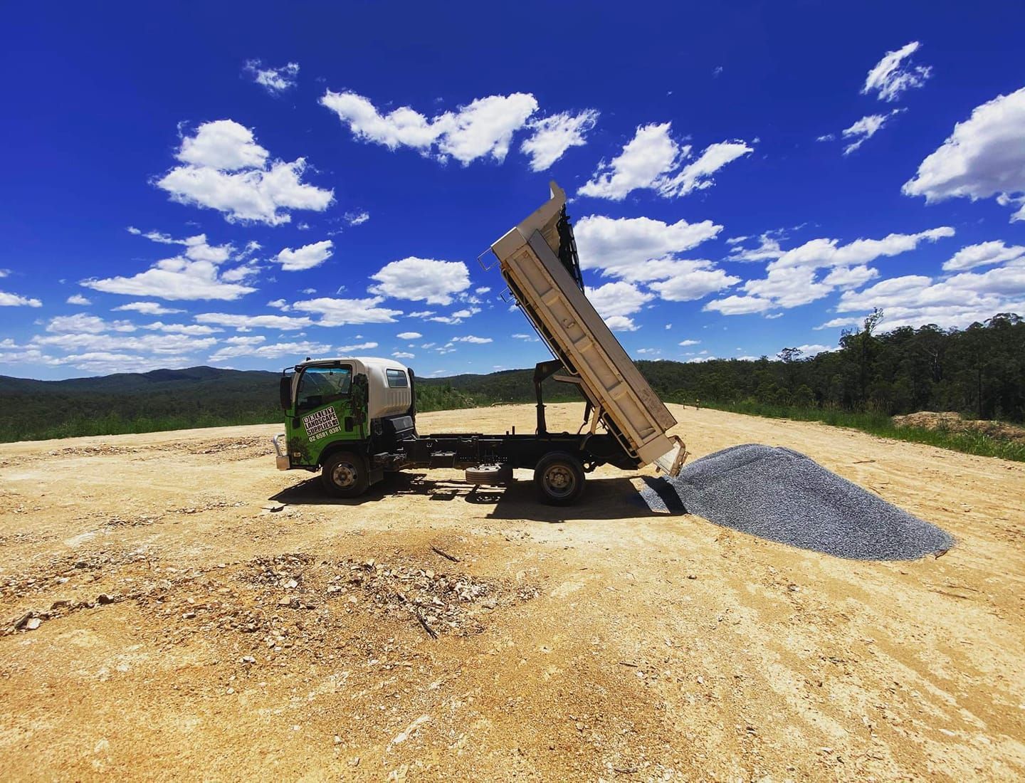 Dump Truck Unloading Gravel on A Dirt Road, Under a Blue Sky with Clouds — Port Landscape Supplies in Port Macquarie, NSW