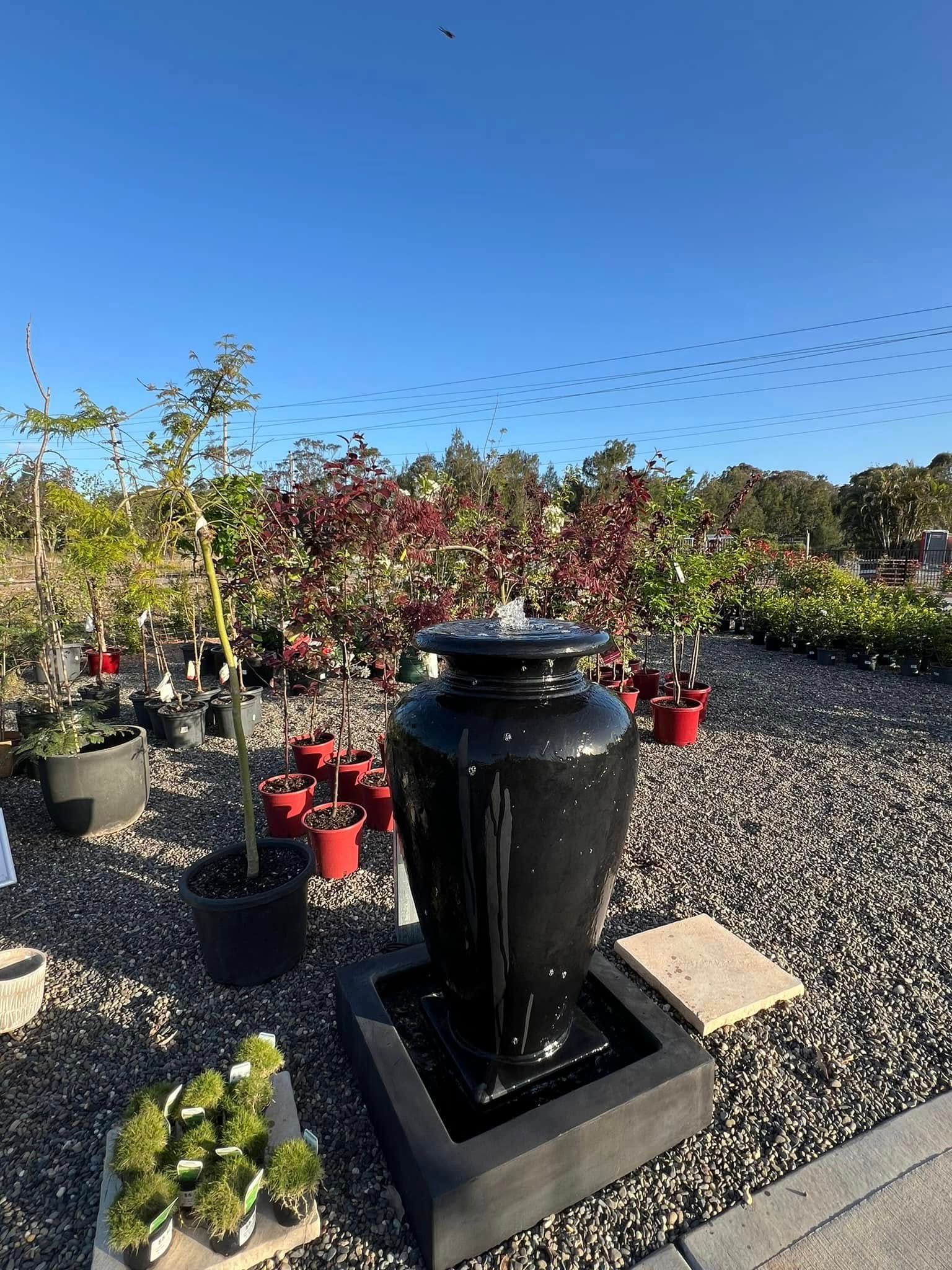 Black Ceramic Fountain in A Garden Center, Surrounded by Plants and Blue Sky — Port Landscape Supplies in Port Macquarie, NSW