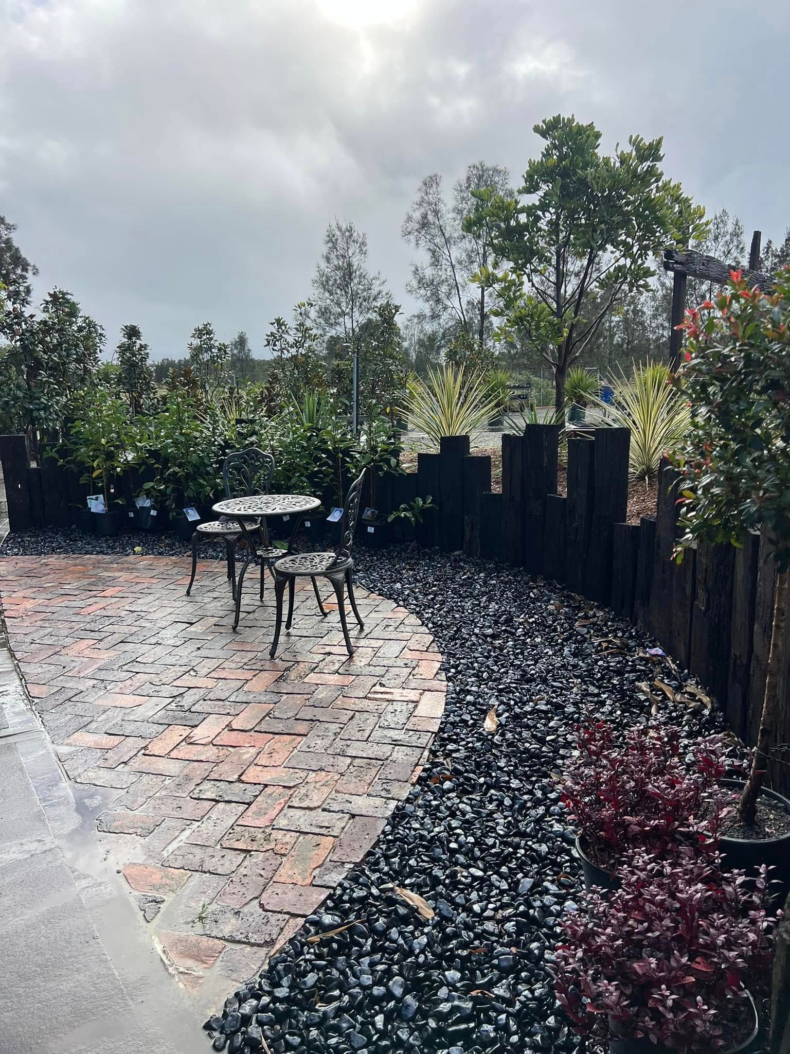 Patio with brick and black rock path, metal table and chairs, trees & plants — Port Landscape Supplies in Port Macquarie, NSW