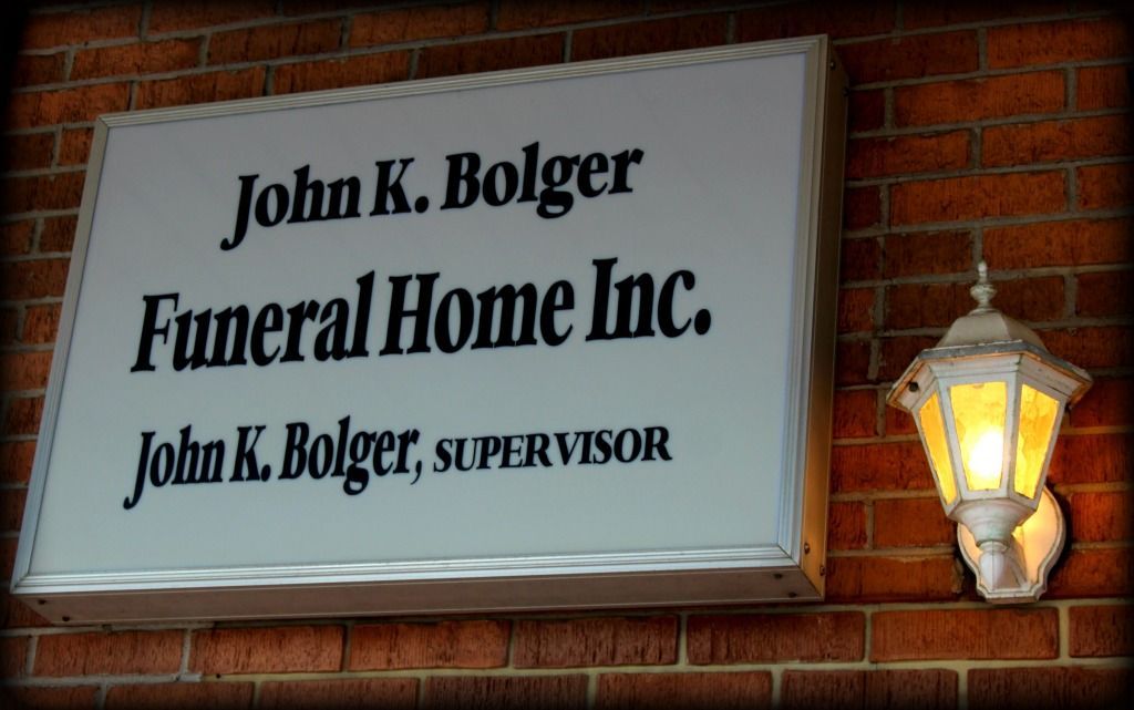 Sign for John K. Bolger Funeral Home Inc. on a brick wall, with a lit lantern beside it.