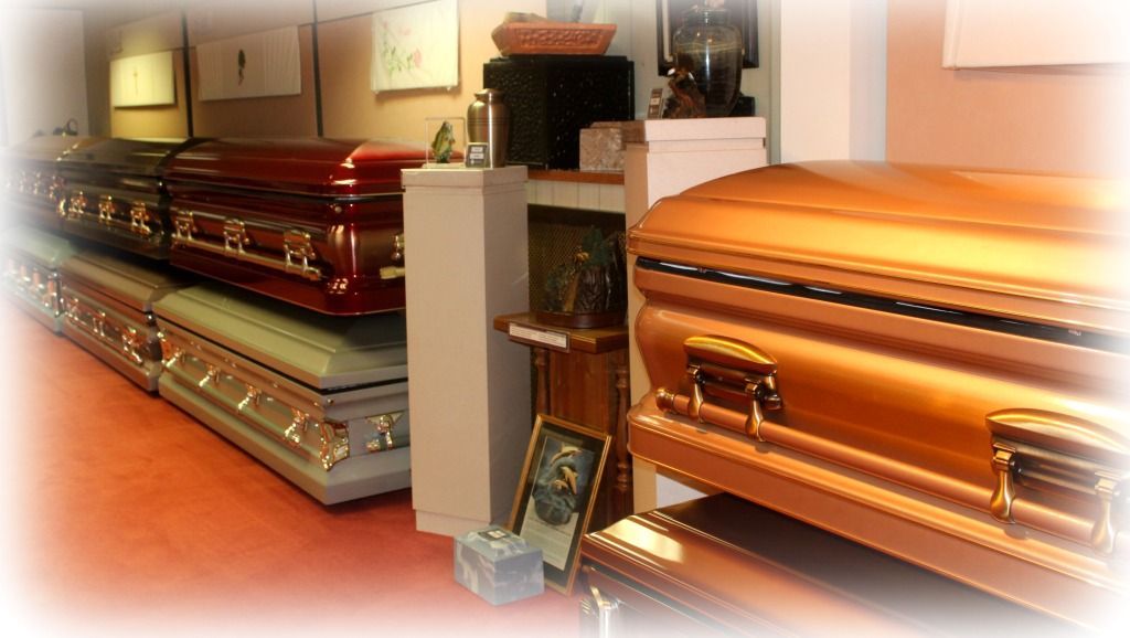 Display of various colored coffins in a funeral home setting.