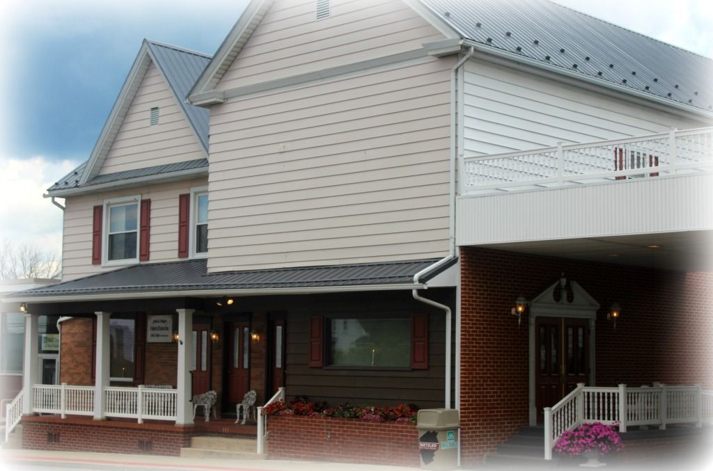 Two-story building with brown brick, tan siding, and a porch with white railings and a dark roof.