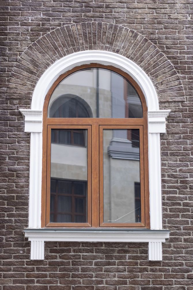 Finestra ad arco in legno con cornice bianca incastonata in una parete di mattoni di un edificio.
