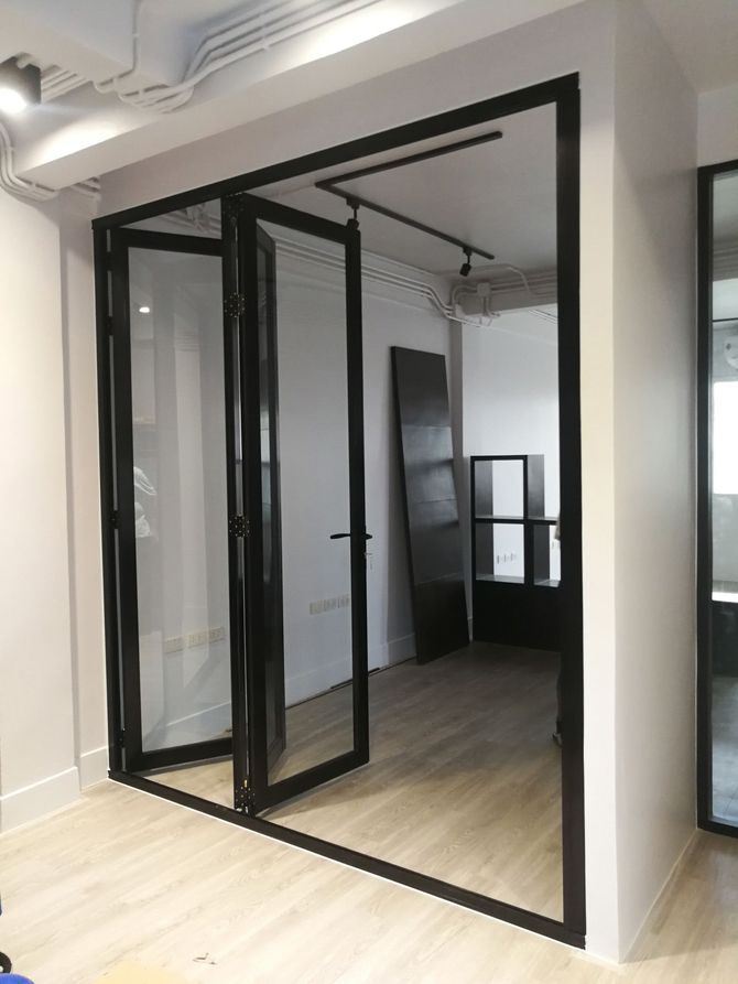 Ufficio con pareti in vetro, porte con telaio nero e pavimento in legno chiaro, in un ambiente moderno.