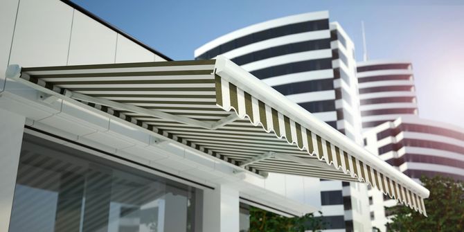 Edificio moderno con tenda a strisce e balconi in vetro curvo contro un cielo luminoso