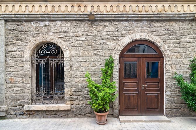 Facciata dell'edificio in pietra con finestra ad arco, porta in legno e piante in vaso sul davanti.