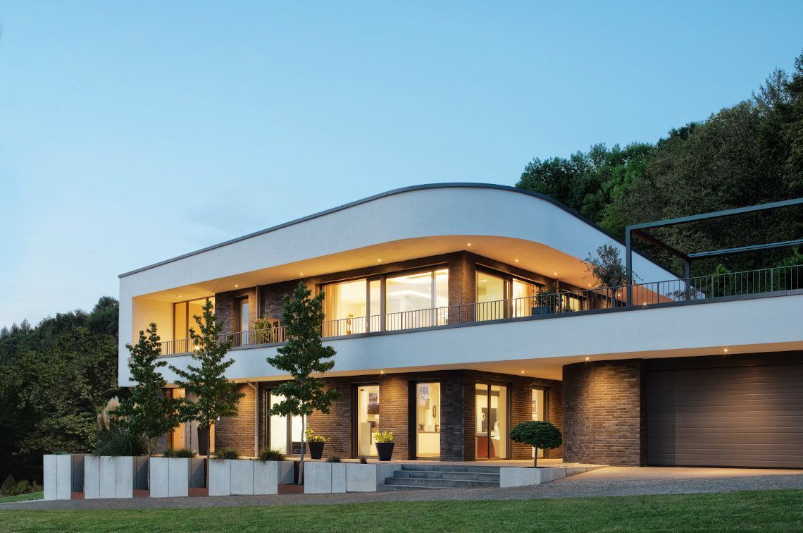 Casa moderna a due piani con luci interne calde, tetto bianco e facciata in mattoni al crepuscolo
