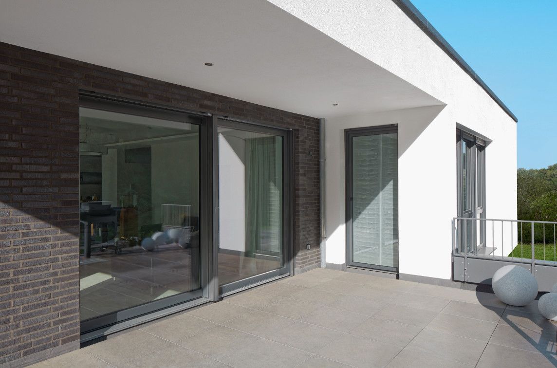 Patio moderno con ampie porte scorrevoli in vetro, pareti bianche, dettagli in mattoni e piante in vaso.