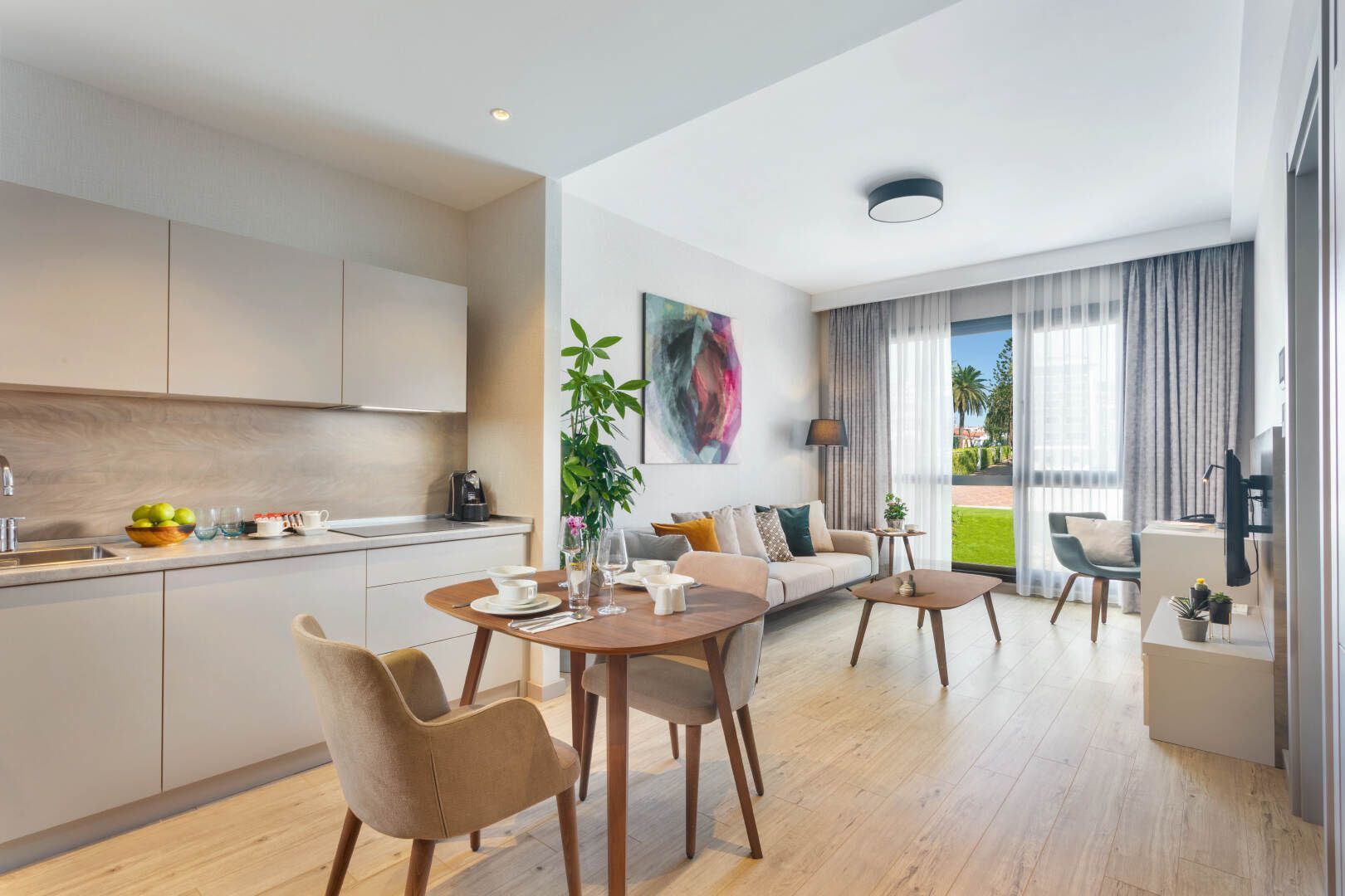 Luminoso e moderno soggiorno-cucina a pianta aperta con tavolo da pranzo, divano, ampia finestra e vista dal balcone.