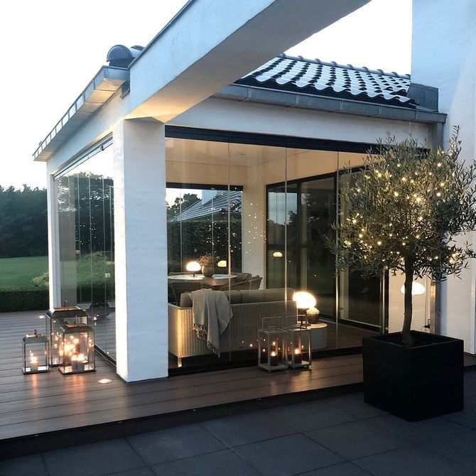Patio moderno con pareti in vetro, colonne bianche, lanterne e un albero in vaso al crepuscolo