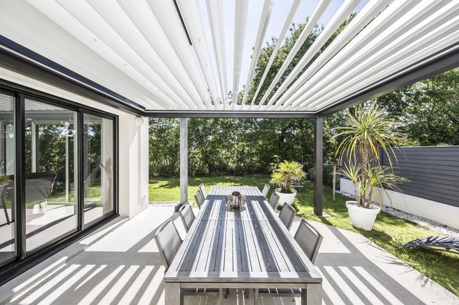 Patio moderno con pergola, tavolo da pranzo e ombre a strisce in un luminoso giardino sul retro.