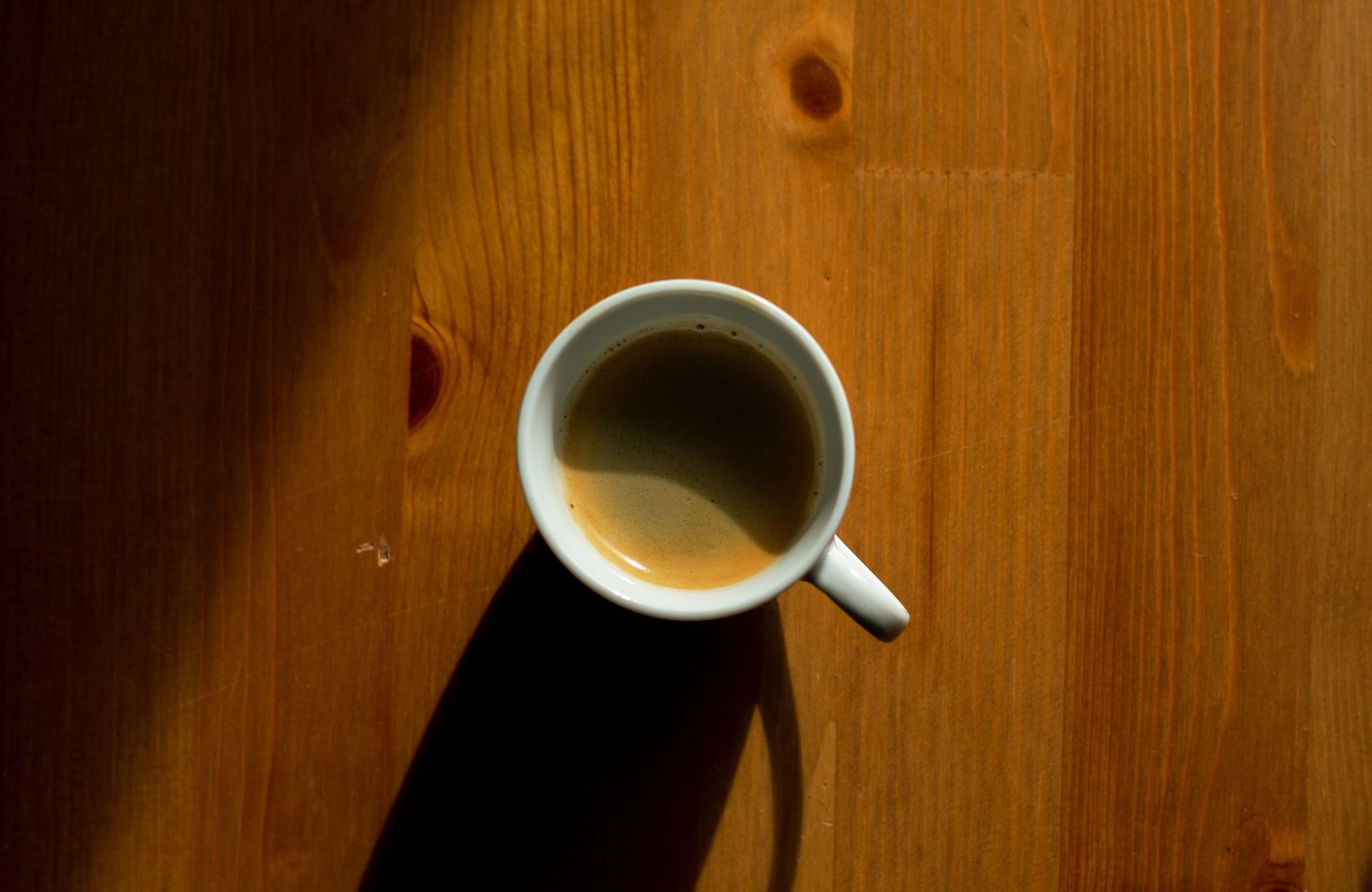 White cup of black coffee on a sunlit wooden table — illustrative photo