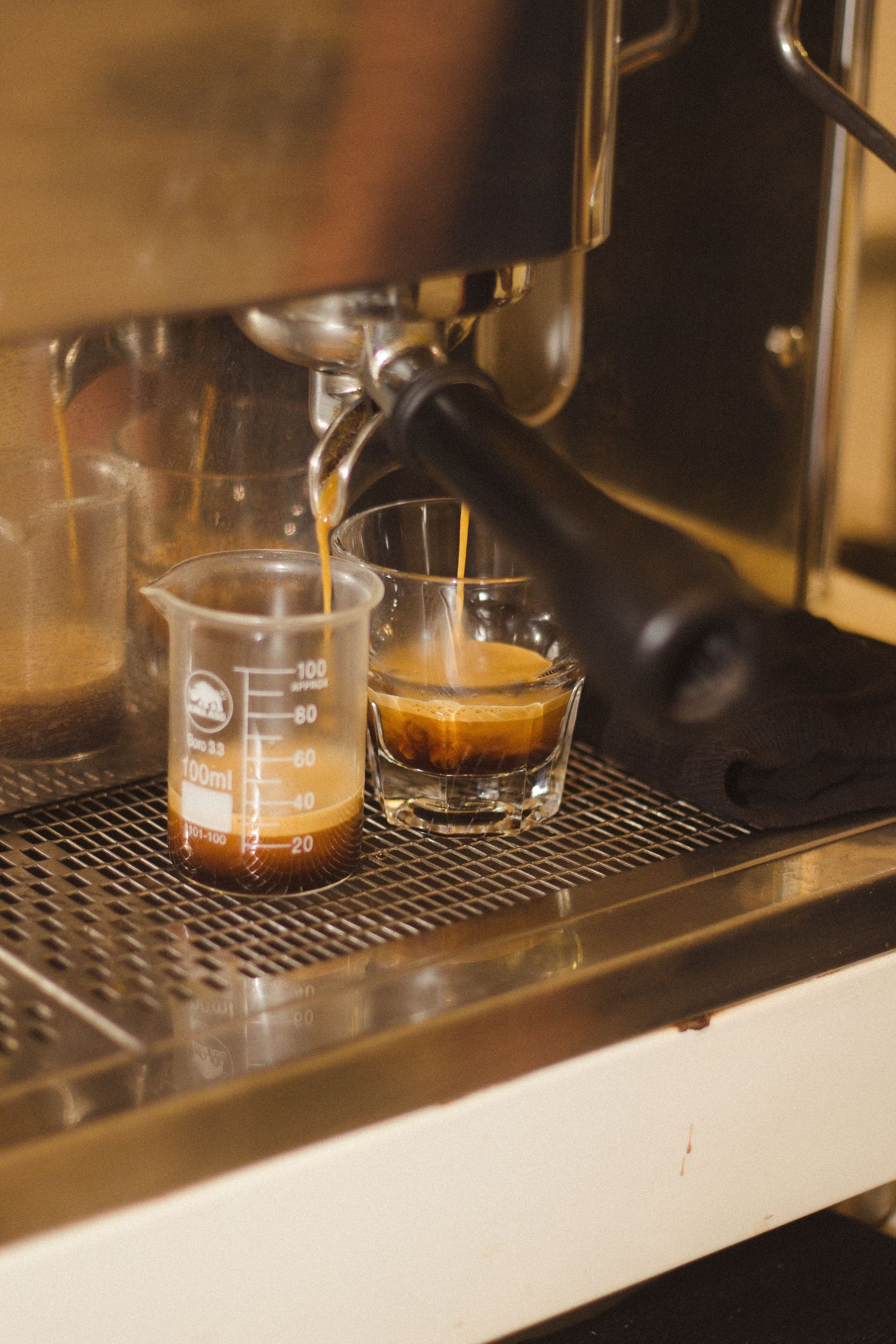 Espresso pouring into two clear glasses beneath a coffee machine — illustrative photo