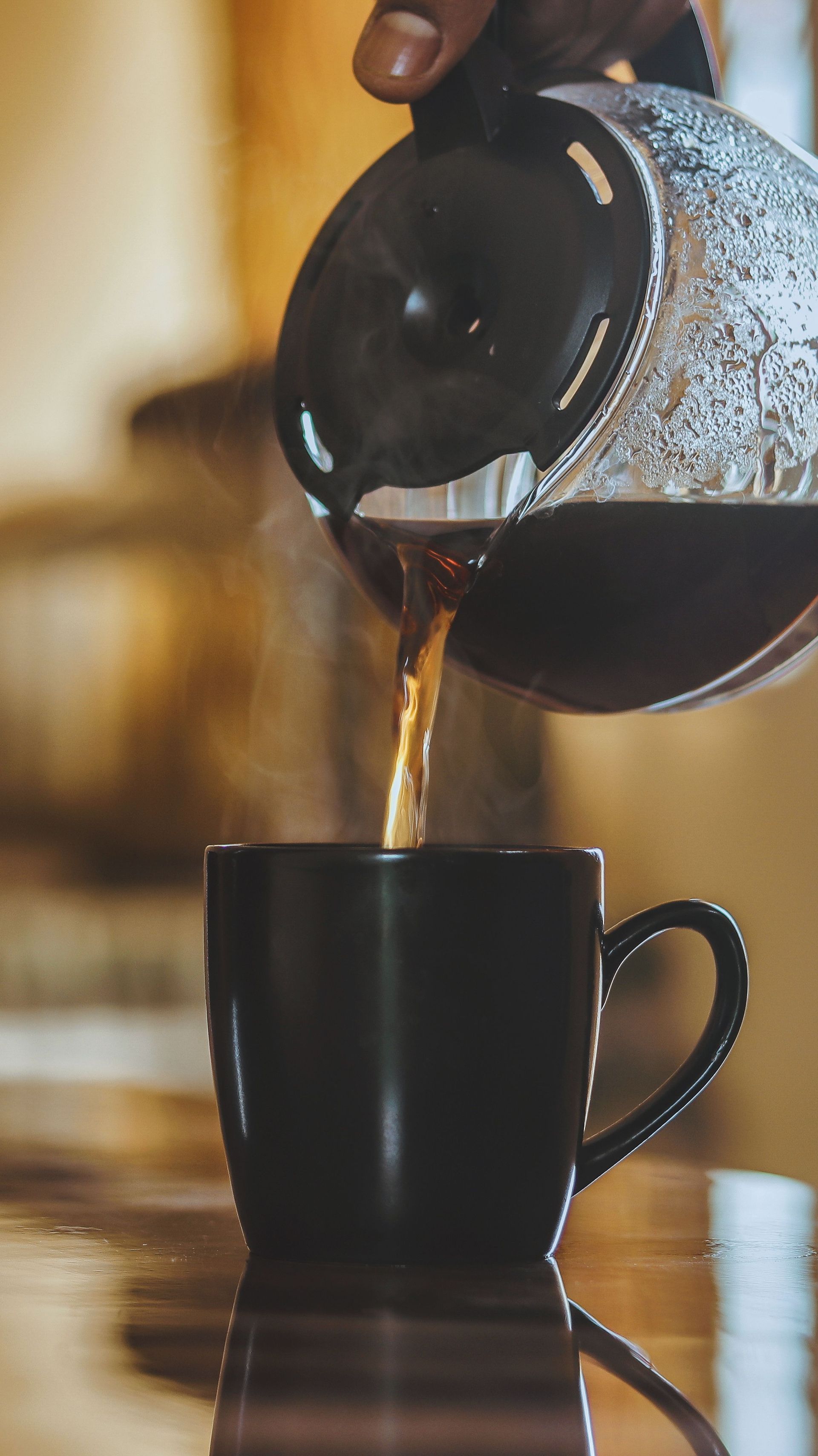 Coffee pouring from a glass carafe into a dark mug — illustrative photo