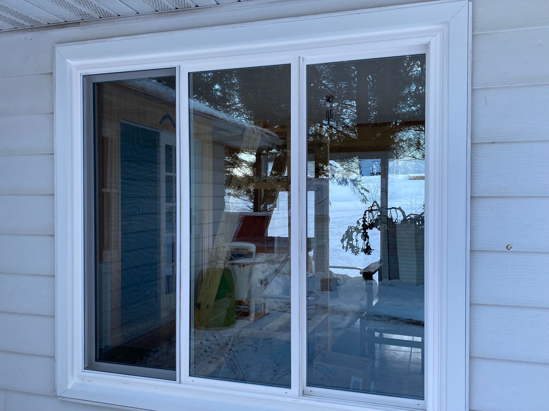 White-framed sliding glass window on a light blue house exterior, reflecting outdoor scene with snow. White-framed sliding glass window on a light blue house exterior, reflecting outdoor scene with snow.