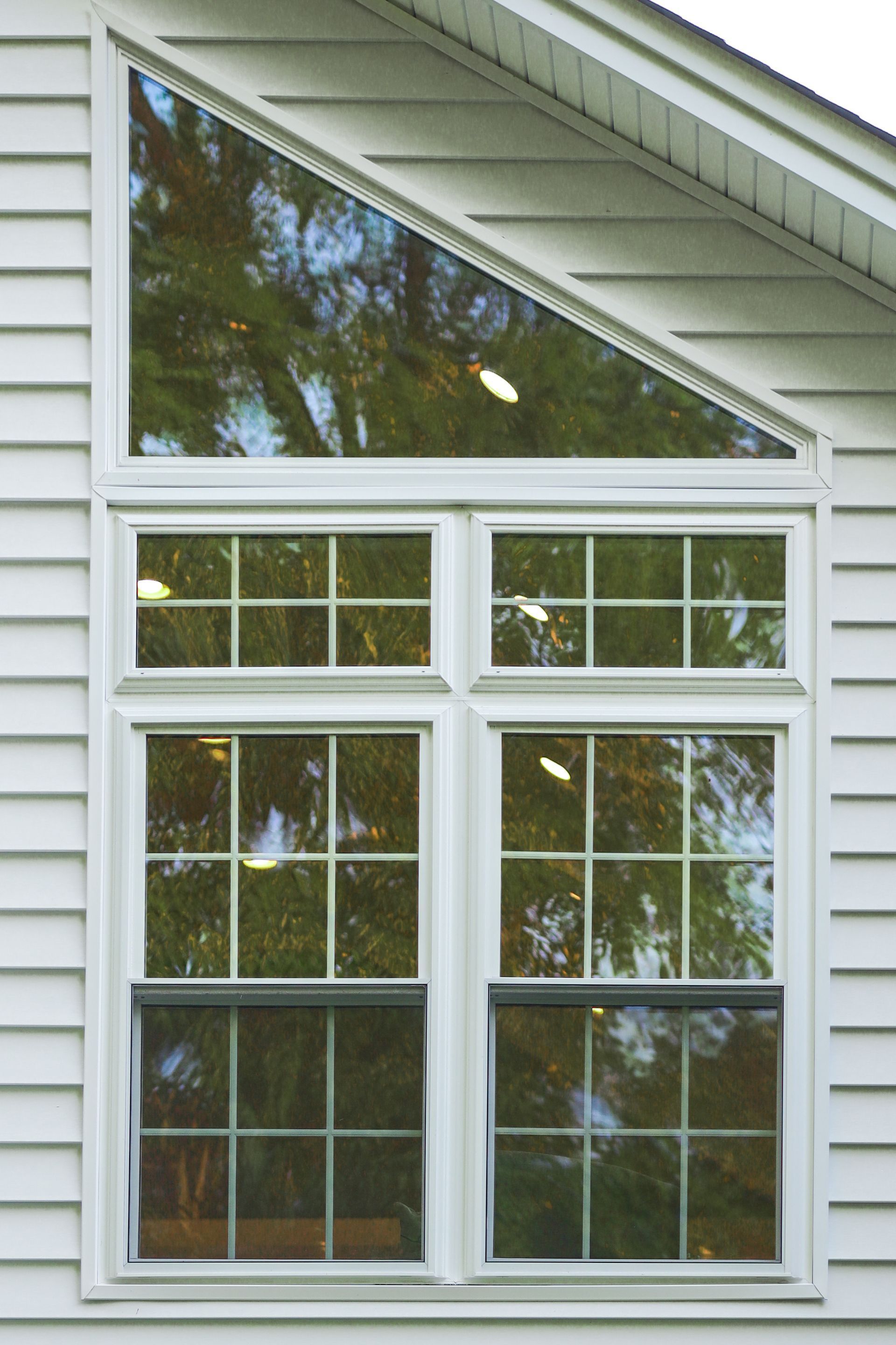 White house with a large window consisting of a triangular pane above two pairs of rectangular panes, reflecting trees. White house with a large window consisting of a triangular pane above two pairs of rectangular panes, reflecting trees.