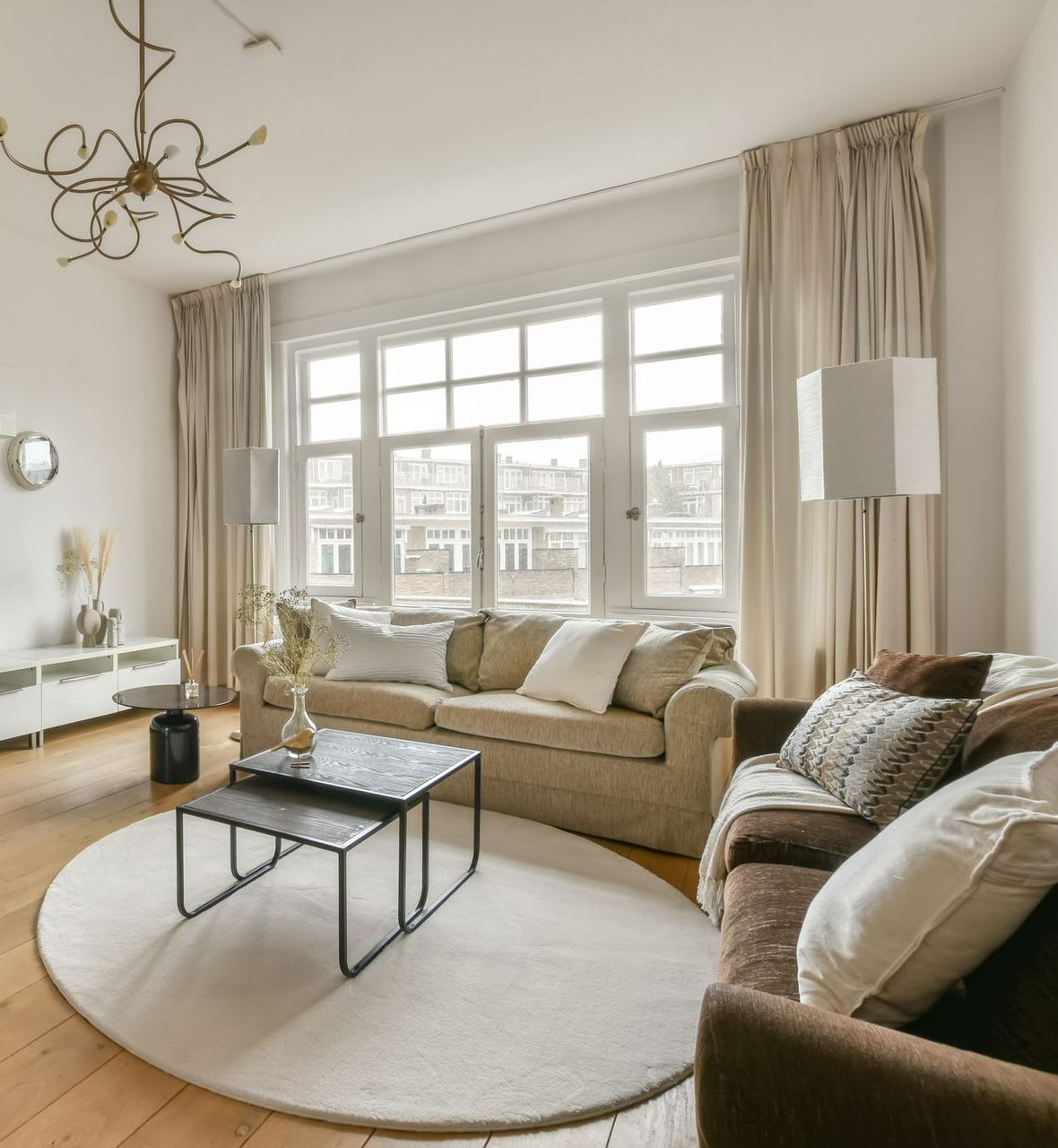 Living room with beige sofa, brown armchair, round rug, and window with curtains.