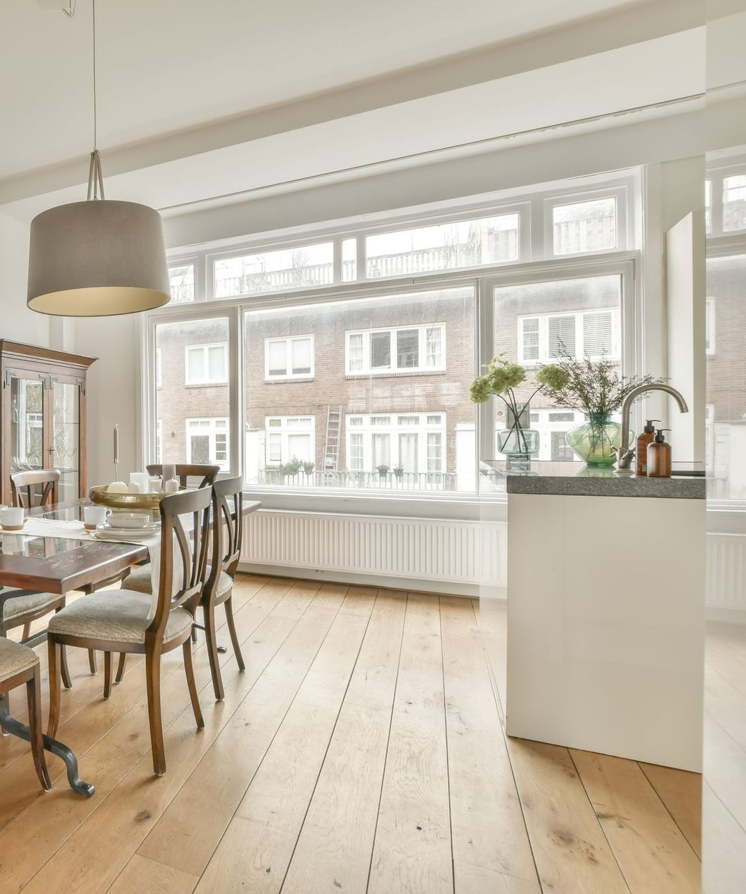 Dining room with wood floor and large window overlooking building; table and chairs. Dining room with wood floor and large window overlooking building; table and chairs.