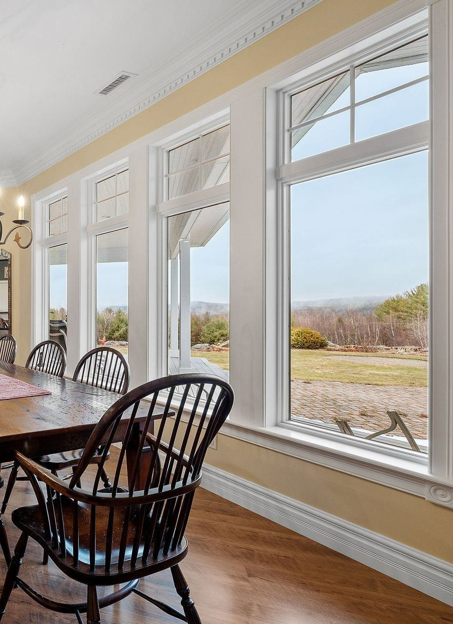 Dining room with wooden table and chairs, large windows overlooking a grassy landscape. Dining room with wooden table and chairs, large windows overlooking a grassy landscape.