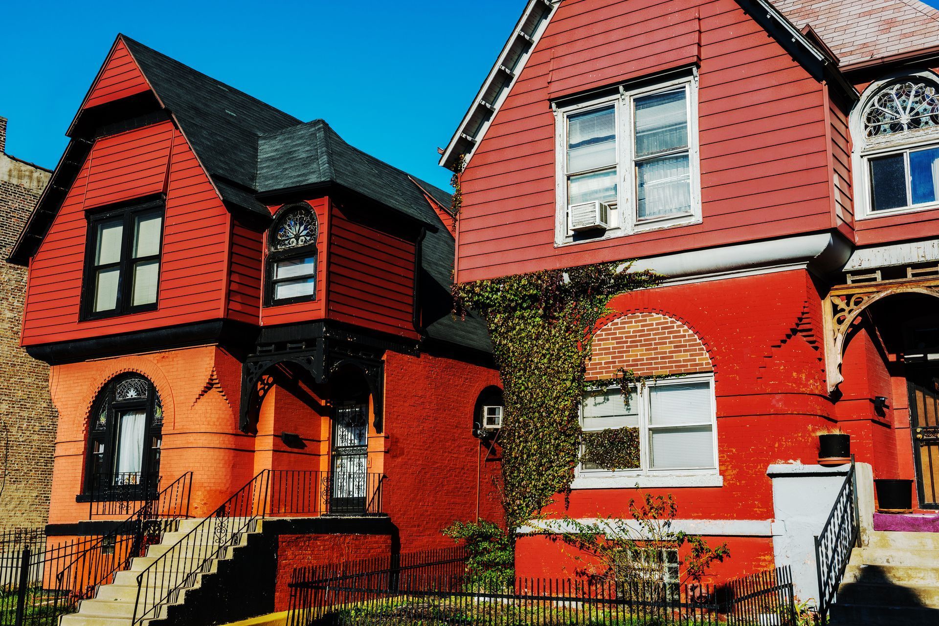 Red and orange Victorian-style houses with dark trim under a clear blue sky.