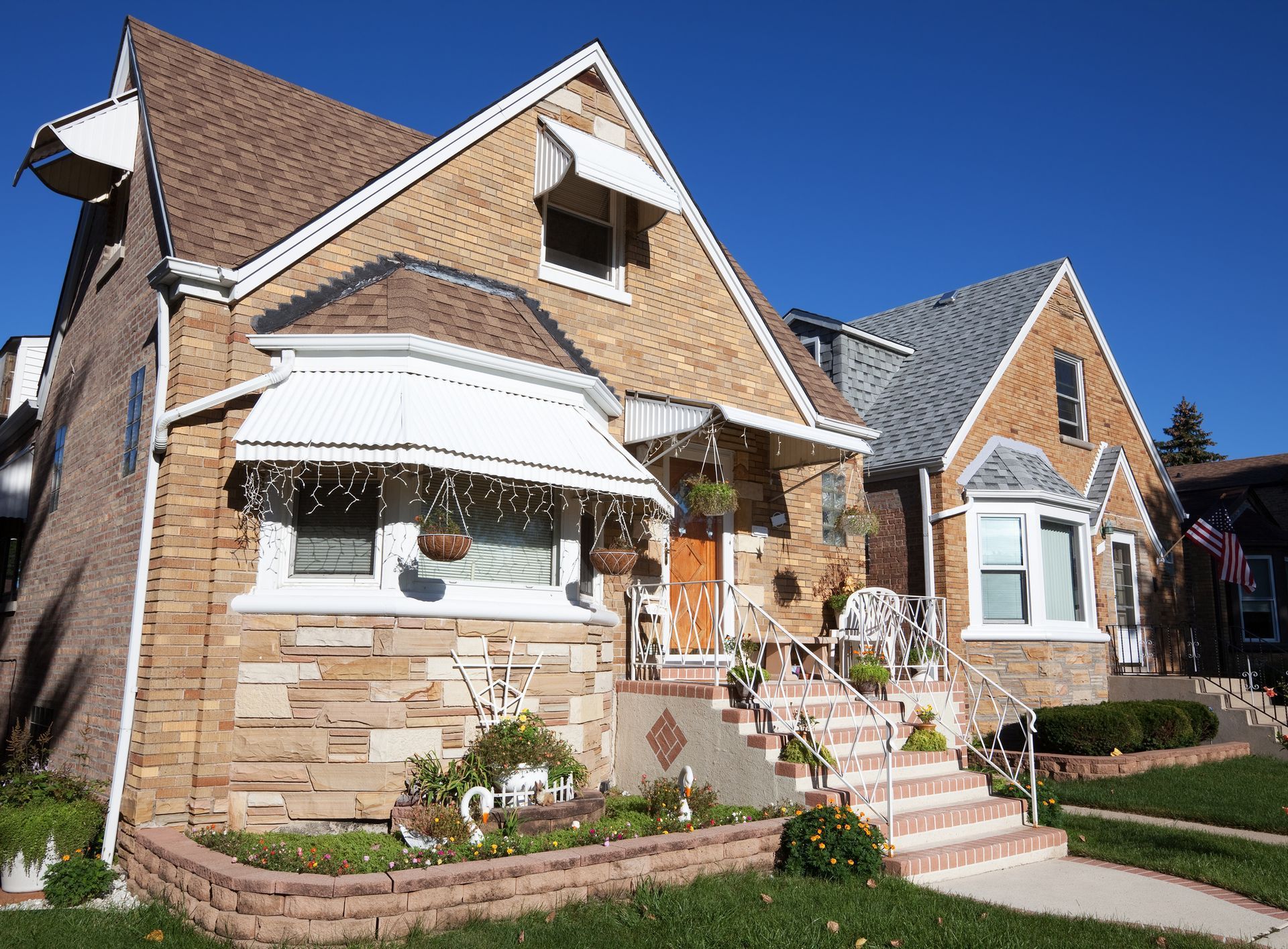 Two-story brick houses with gabled roofs and awnings against a clear blue sky.