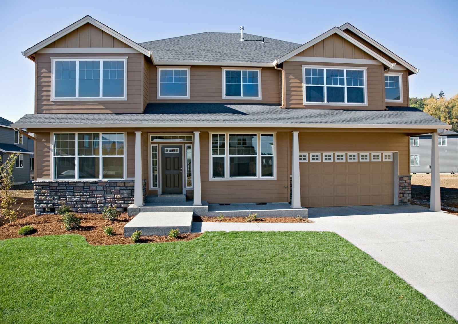 Two-story house with brown siding, a dark roof, a stone accent, and a green lawn. Two-story house with brown siding, a dark roof, a stone accent, and a green lawn.