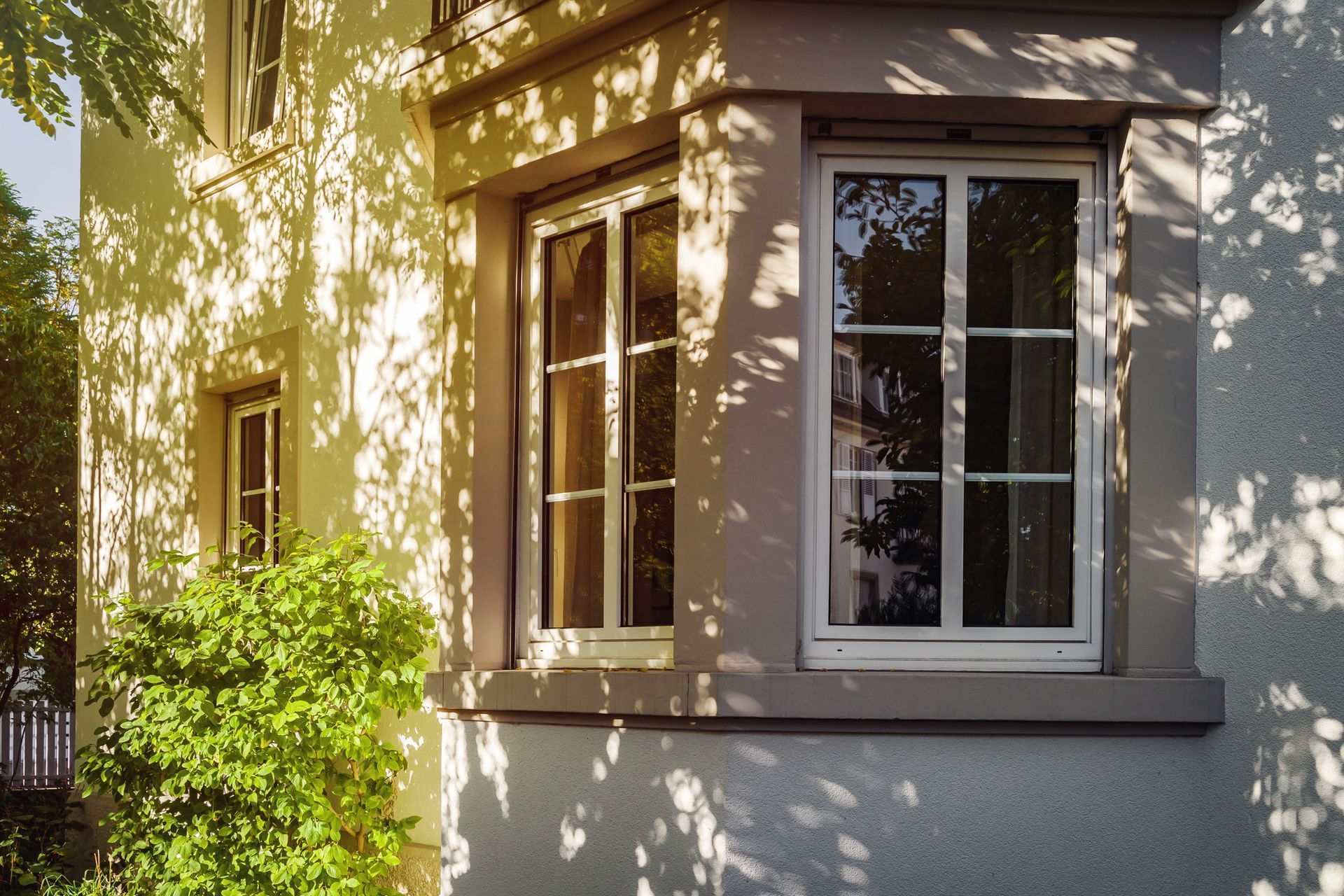 House exterior with sunlight casting shadows on the white stucco walls and windows with white frames.