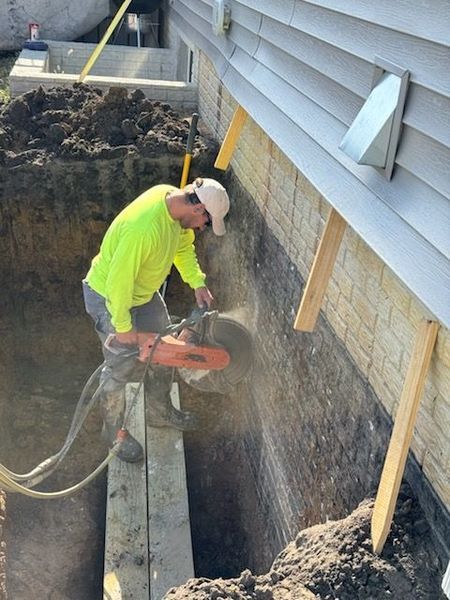 Man in neon shirt using a concrete saw on a brick wall, outdoor construction site.