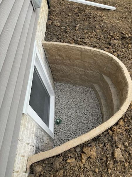 Window well with beige retaining wall, gravel floor, and house siding.