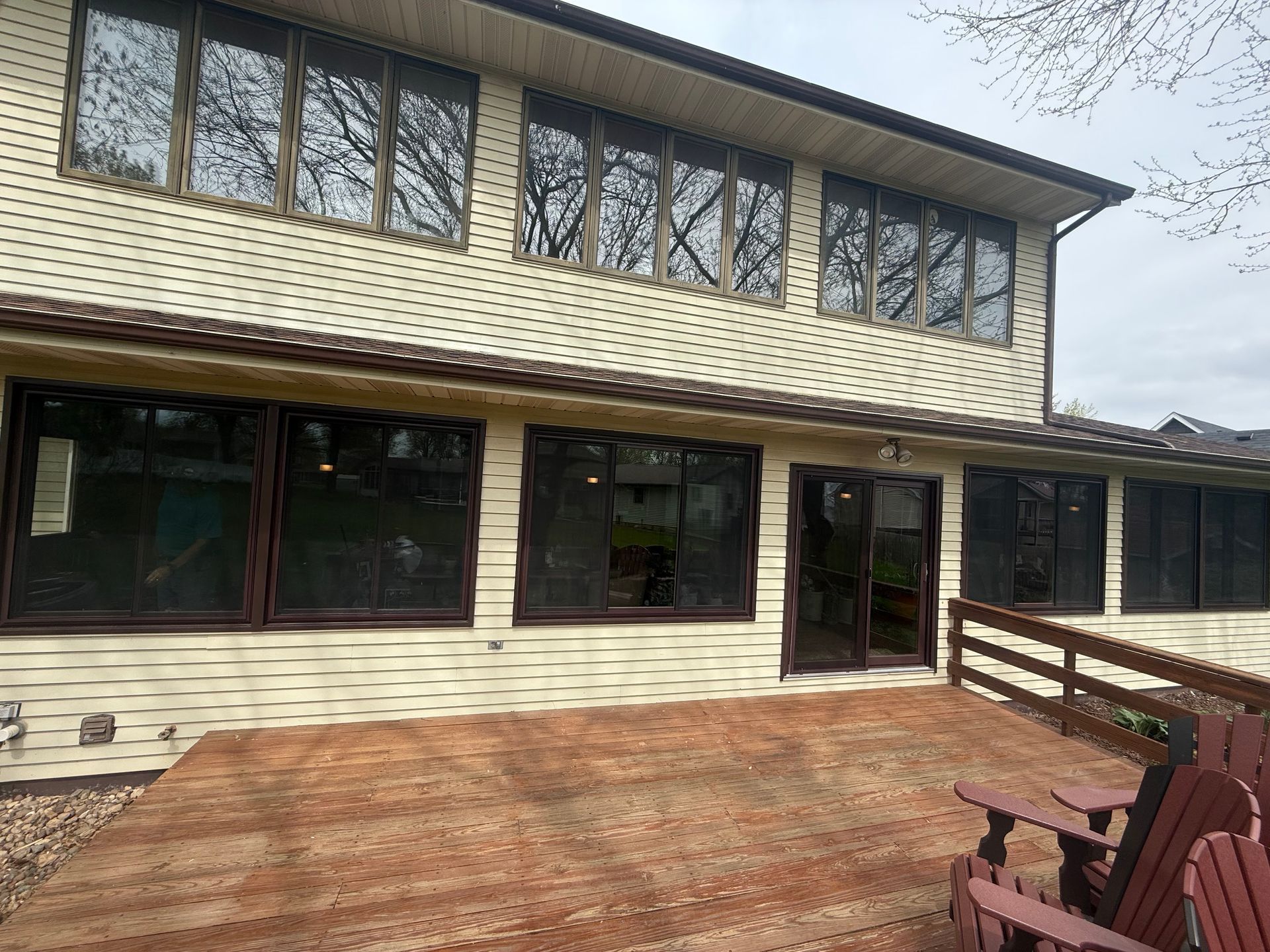Beige house with brown-framed windows, overlooking a weathered wooden deck with Adirondack chairs. Beige house with brown-framed windows, overlooking a weathered wooden deck with Adirondack chairs.