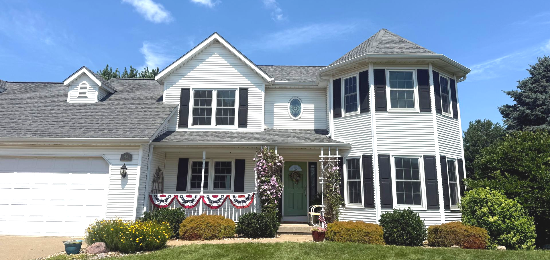 White two-story house with a rounded side, black shutters, and a blue door, against a clear sky. White two-story house with a rounded side, black shutters, and a blue door, against a clear sky.