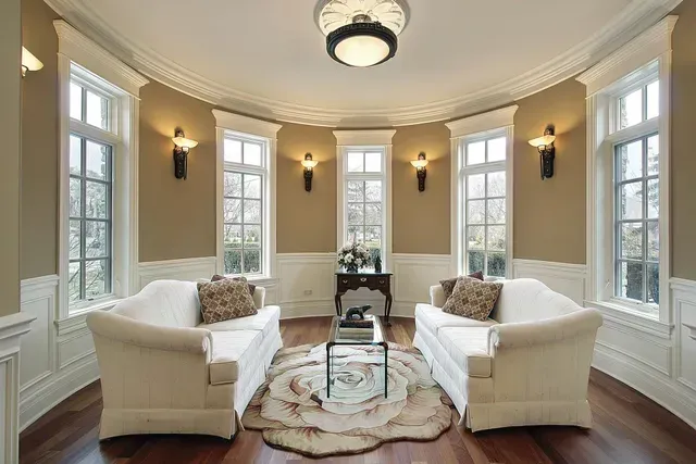 Curved room with two white sofas, windows, and sconces. Features a glass table on a rug.