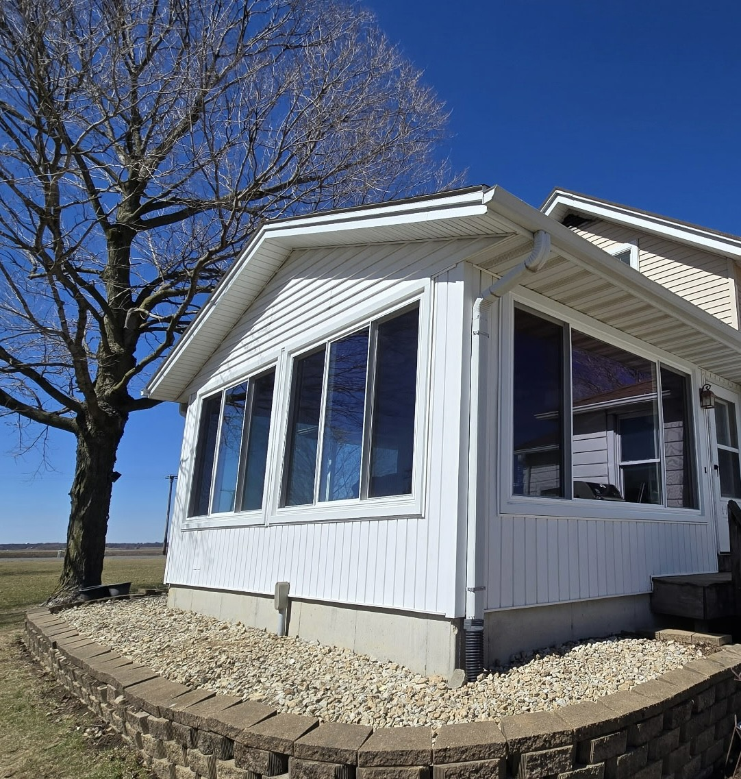 White house with large windows, leafless tree, gravel bed, and blue sky. White house with large windows, leafless tree, gravel bed, and blue sky.