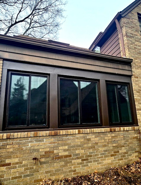 Brown-framed windows on a brick building with a brown roof trim against a cloudy sky.