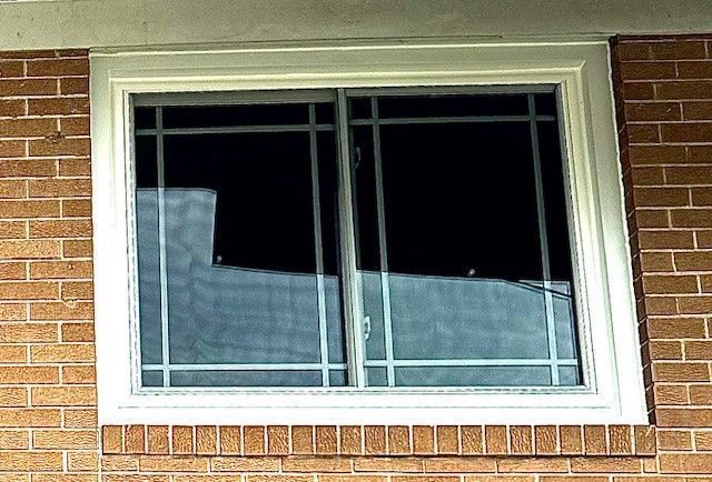 White-framed sliding window with white grilles, set in a brick wall.