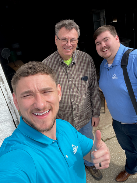 Three men smile, two indoors. One gives a thumbs-up. The man closest is wearing a blue polo.