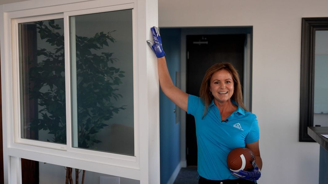 Woman in blue shirt holding football, cleaning window frame with a gloved hand.
