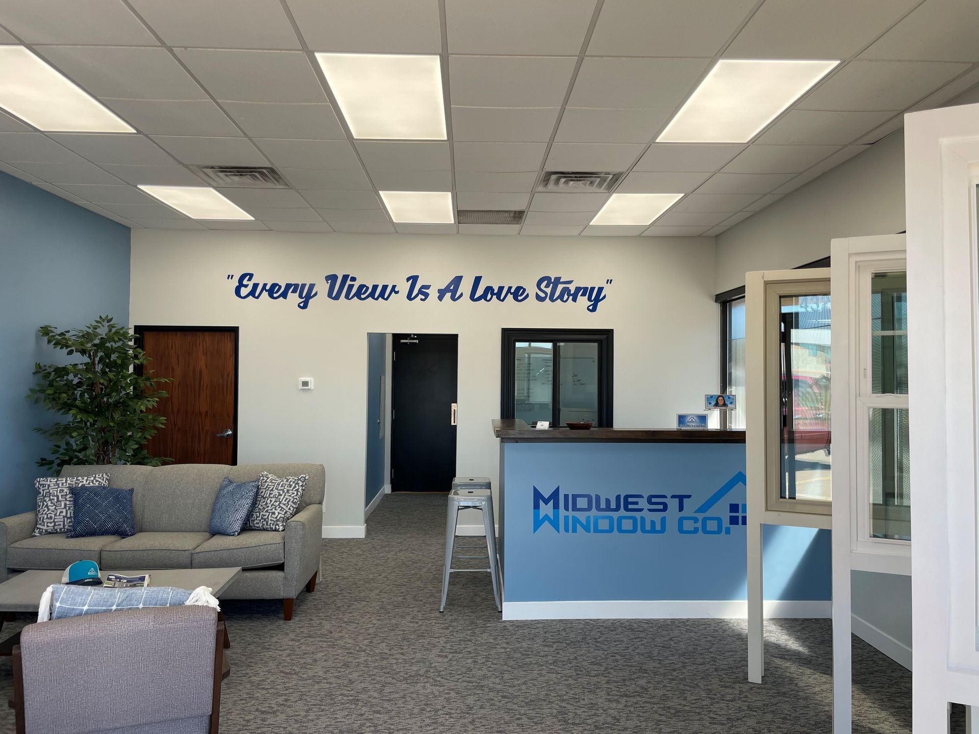 Interior of a Midwest Window Co. showroom with blue walls, a gray sofa, and a reception desk. Interior of a Midwest Window Co. showroom with blue walls, a gray sofa, and a reception desk.