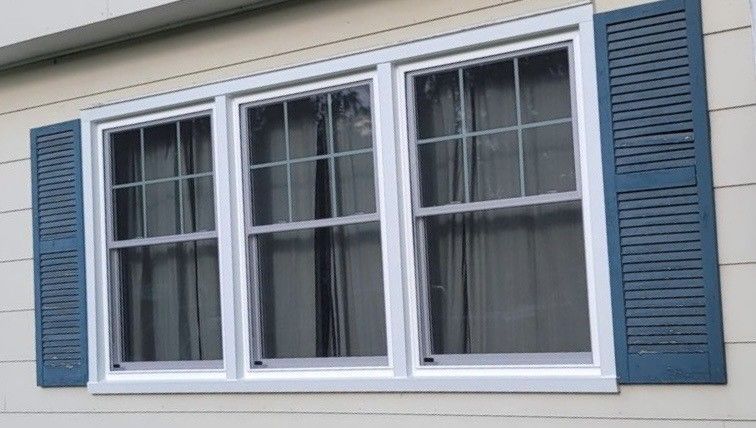 Three white-framed windows with dark blue shutters on a cream-colored house.