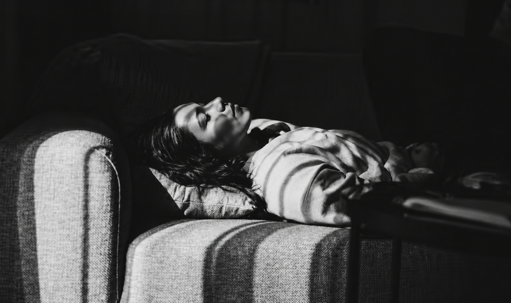Woman with nausea after surgery resting on a sofa while waiting for in-home IV therapy.