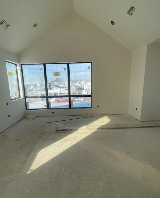 The interior of a home with tall windows, an angled ceiling, a bare subfloor, and smooth white walls.
