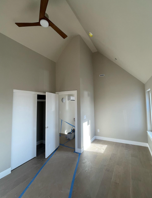The interior of a home with gray walls, a white closet door, wood plank flooring, and a ceiling fan.