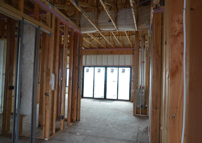 The inside of a building with a subfloor, wood ceiling beams, studs, and glass doors covered with a protective film.