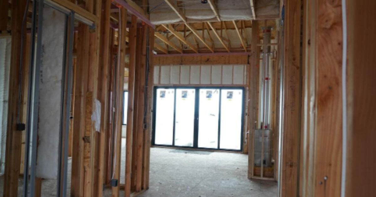 An unfinished room with exposed wall studs, ceiling joists, metal framing, and tall glass doors.