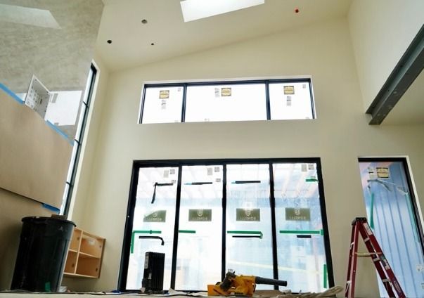 A bright unfinished room with tall black-framed windows, glass doors, a red ladder, tools, and const