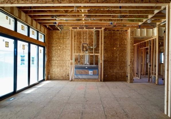 An unfinished interior with exposed wood framing, ceiling joists, large black-framed glass doors, ductwork, and bare floors.