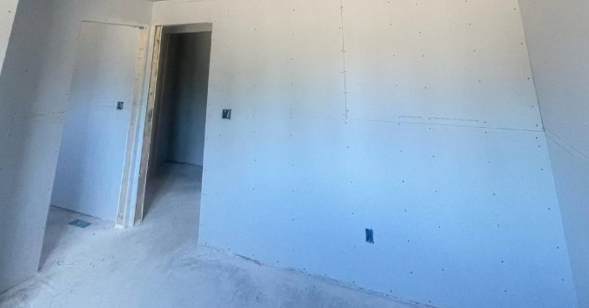 An unfinished room with freshly installed drywall, a doorway opening, and construction dust on the floor.