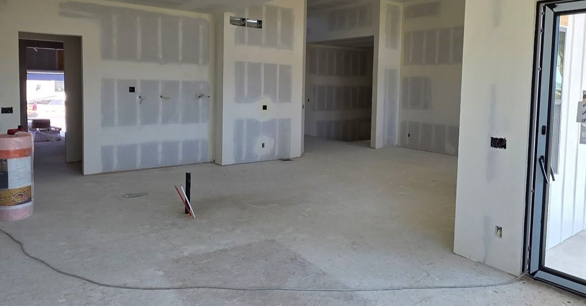 An unfinished interior with taped drywall, square columns, exposed outlets, and a sliding glass door beside a concrete floor.