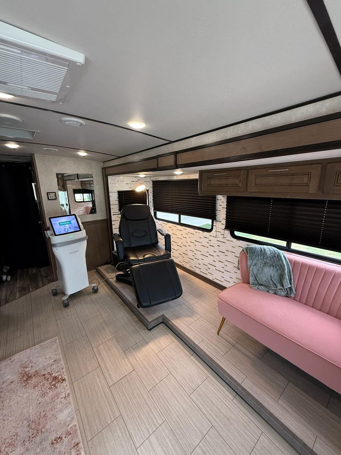 Modern RV interior with a black seat, pink bench, wood cabinets, and a small standing desk monitor