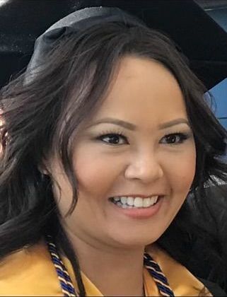 A woman wearing a graduation cap and gown is smiling